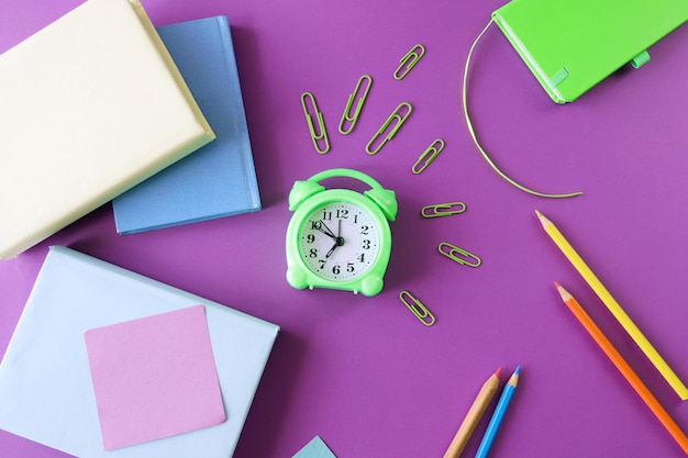 Stationery and an alarm clock pencils and books on a purple background the concept of learning