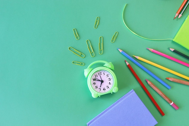 Stationery and alarm clock pencils pastel colored paper on a green background top view