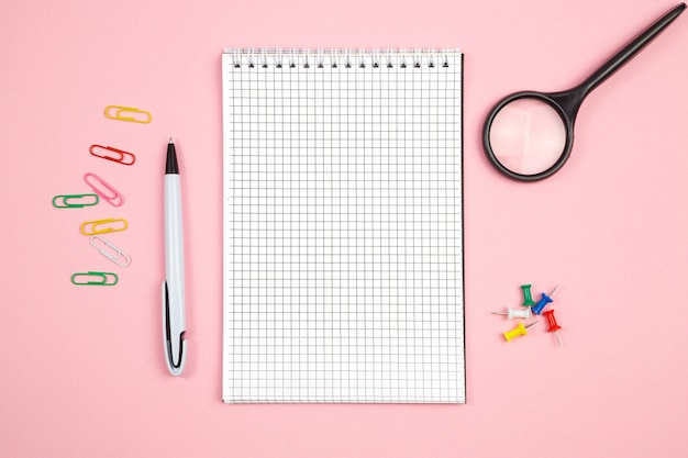 Stationery, paper notebook with pen and magnifier on pink isolated background. top view. flat lay. mockup