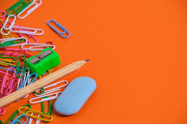 Stationery for schoolchildren paper clips pencil eraser and sharpener on an orange background