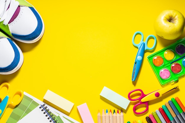 Stationery set, sneakers and apple on bright yellow background top view. Back to school.