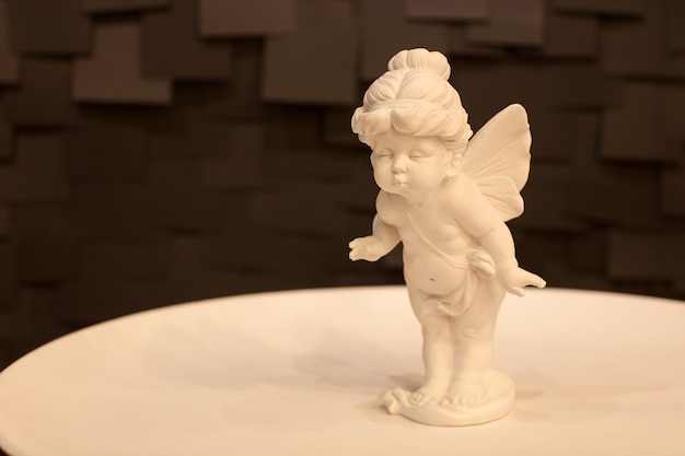 어두운 배경에 흰색 접시에 날개를 가진 천사 소녀의 동상