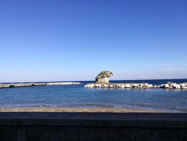 Statue by sea against clear blue sky