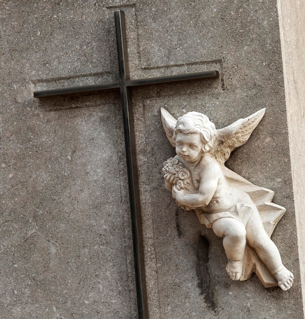 A statue of a cherub holding a cross on a wall.