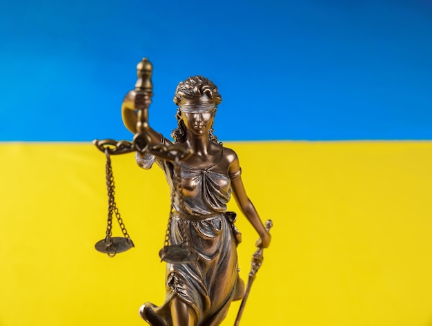 The statue of Lady Justice holding the scales on flag of Ukraine background