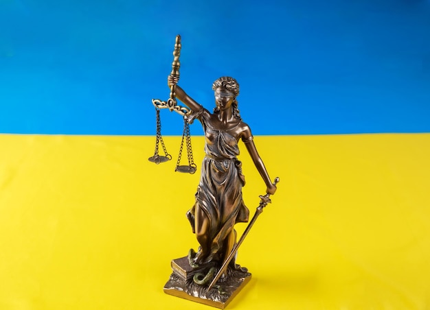 The statue of Lady Justice holding the scales on flag of Ukraine background