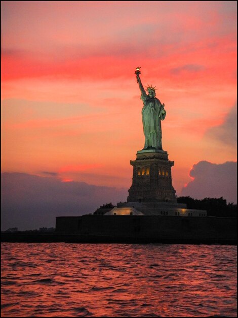 Photo statue of liberty by sea against dramatic sky during sunset