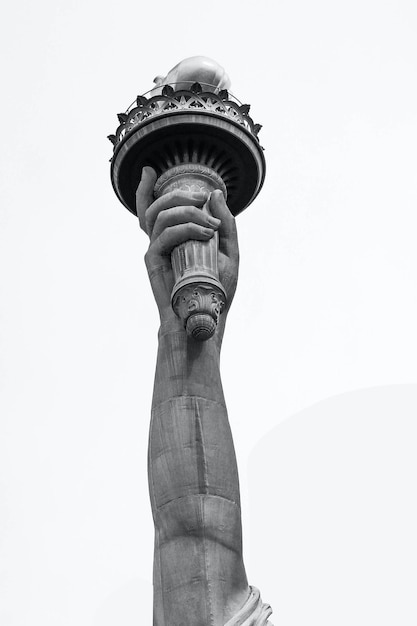 Рука статуи Свободы держит факел на белом фоне