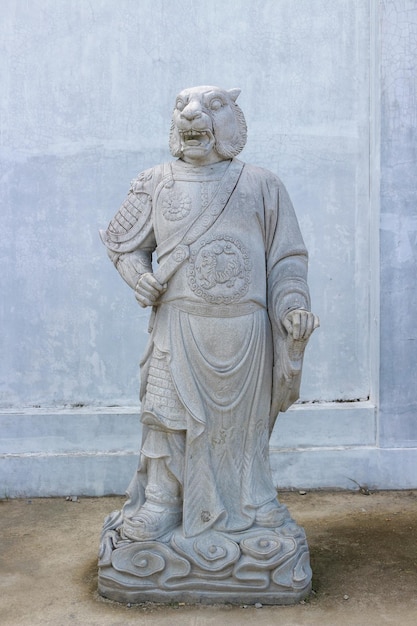 A statue of a lion with a sword in his mouth stands in front of a blue wall.