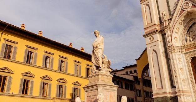 A statue of a man in a robe stands in front of a yellow building.