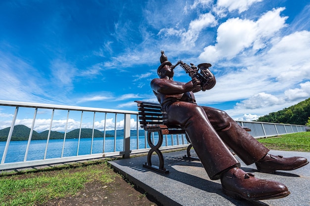 A statue of a man sitting on a bench with a blue sky in the background.