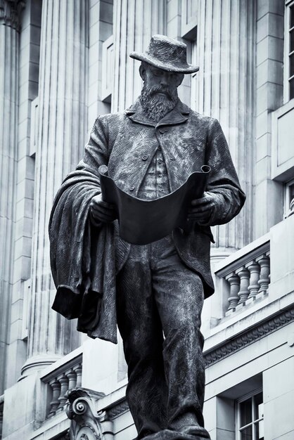 A statue of a man with a hat on and a building behind him.