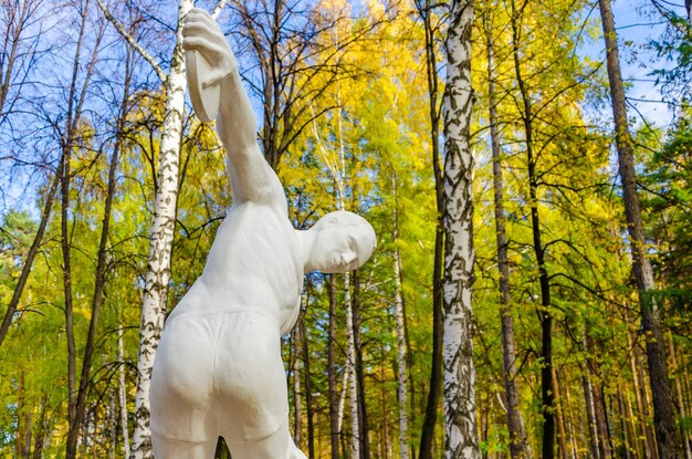 Photo a statue of a man with a white shirt and shorts stands in a forest.