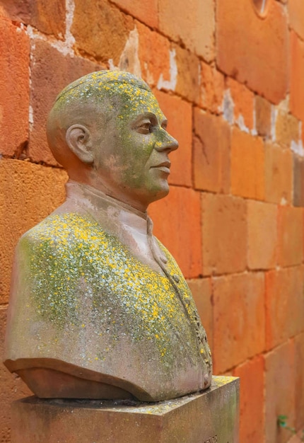 A statue of a man with a yellow paint on it stands in front of a brick wall.