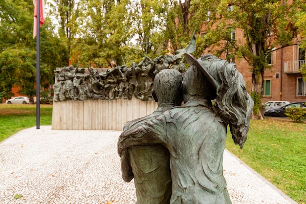 A statue of a man and woman hugging in front of a wall with trees in the background.