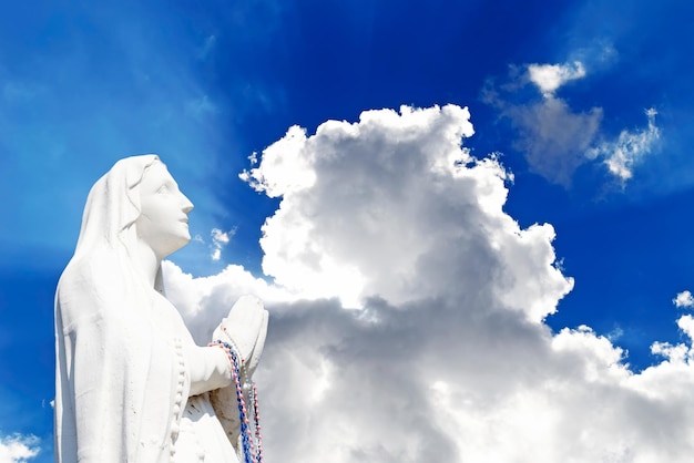 Foto statua di una madonna orante sotto un cielo nuvoloso