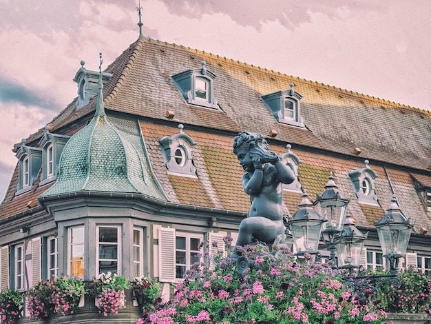 A statue stands in front of a house with flowers