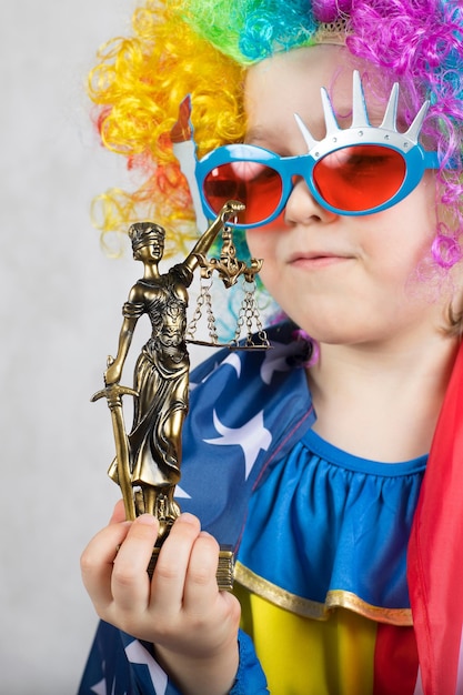 Statue of Themis in the hand of five years old child dressed in clown costume. Closeup