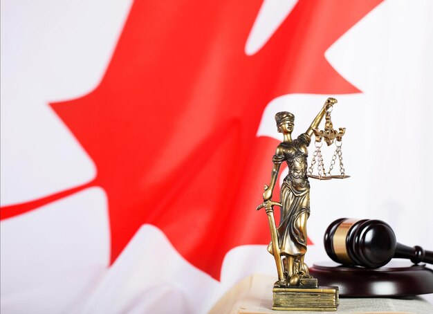 Statue of Themis and judge's gavel on a book. Flag of Canada in the background. Closeup