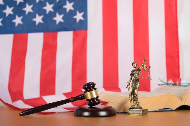 Statue of Themis and judge's gavel on a table. Flag of United States of America in the background.