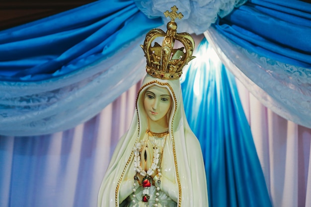 Foto statua della vergine maria e la corona sullo sfondo di una tenda blu