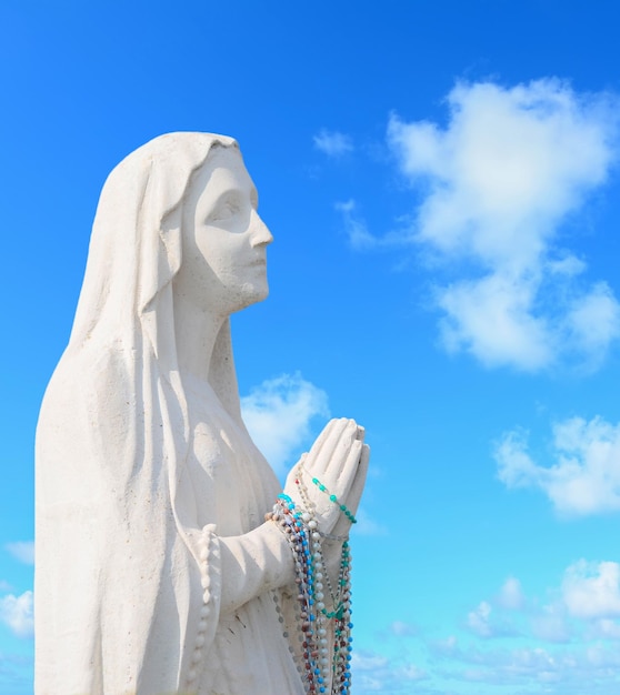 Foto statua della vergine maria che prega sotto un cielo blu