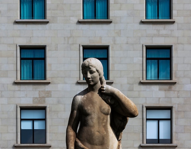 A statue of a woman stands in front of a building with a row of windows.