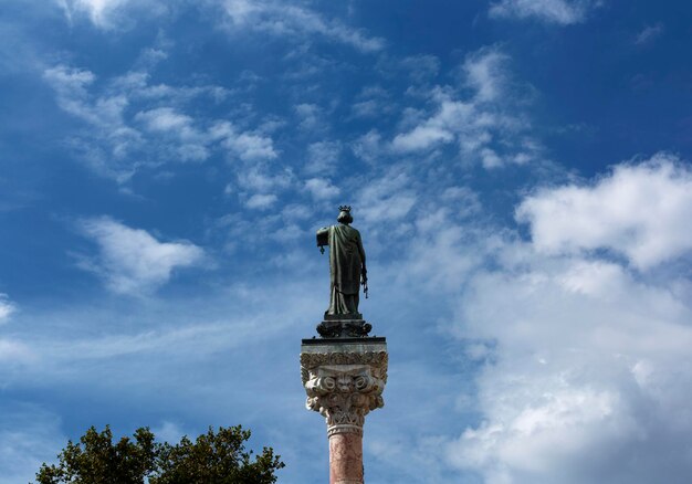 A statue of a woman stands on a pedestal in front of a blue sky.