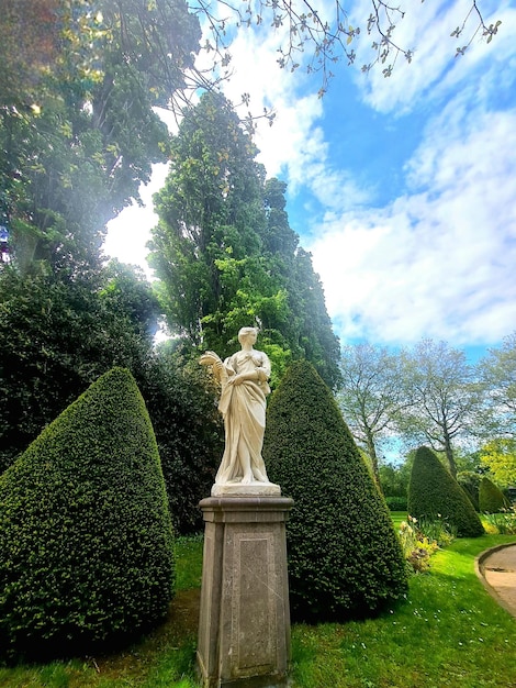 A statue of a woman with a bird on it stands in a garden.