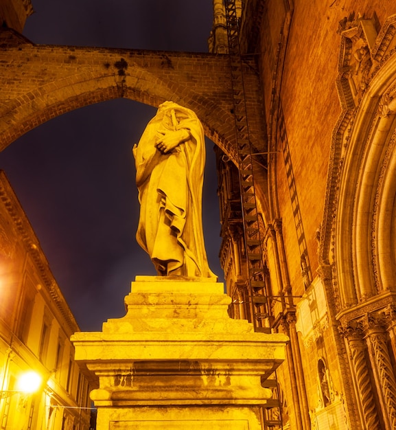 A statue of a woman with a cape on stands in front of a building.