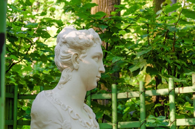 A statue of a woman with a green fence in the background.