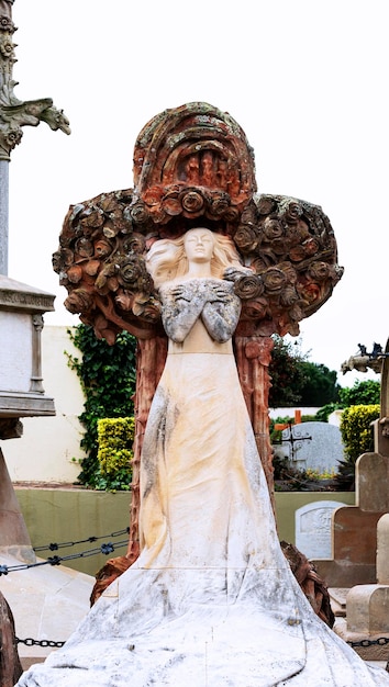 A statue of a woman with a white dress stands in a cemetery.