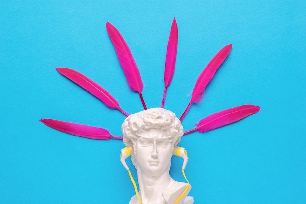 A statuette of Apollo with headphones and bright feathers on the back Minimalism