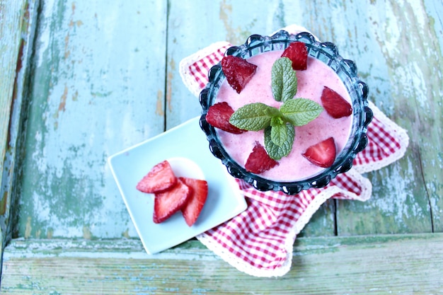 Stawberry smootie with mint decoration in a turqueise glass bowl over a wooden table with copy space