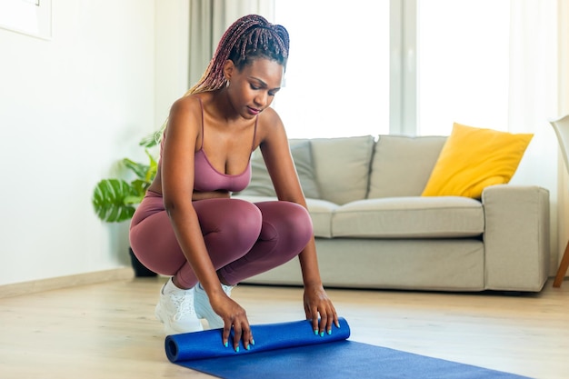 Stay fit concept sporty african american woman rolling yoga mat\
after excercising in living room at home copy space