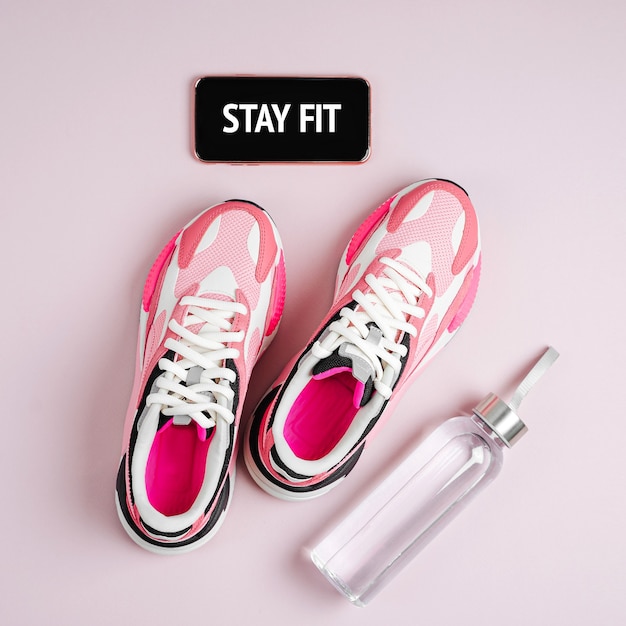 Stay fit. New sneakers and smartphone on a pink background. App for training indoors.