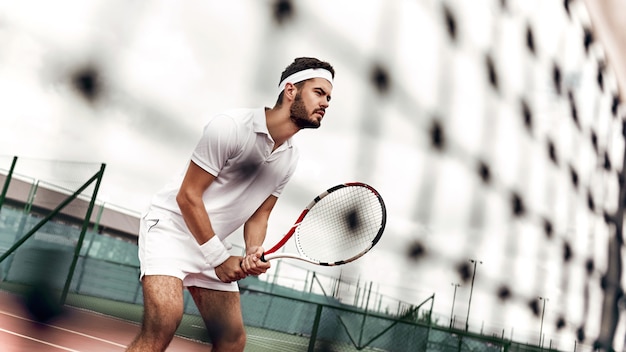 Оставайтесь сосредоточенными, красивый теннисист стоит на корте, готовый к броску