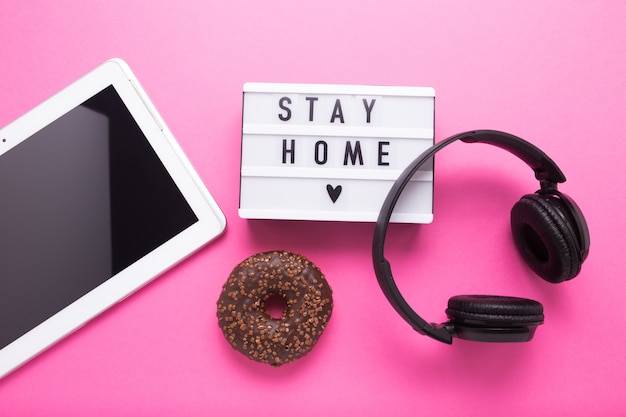 Stay home, boxing inscription. Remote online work at home. Headphones tablet and diary on a pink wall.