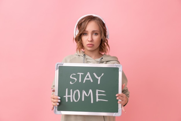 Stay home concept Woman with headphones dressed oversize hoodie holds chalkboard with the words stay home. Coronavirus protection New normal concept Covid19 pandemic Social distancing work from home