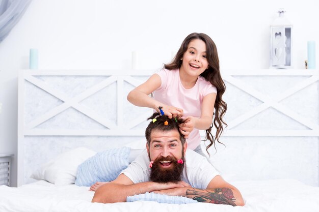 Stay home and have fun family leisure concept girl making\
hairdo for dad quarantine with children happy family pajamas party\
happy childhood relaxing in bedroom affection and support