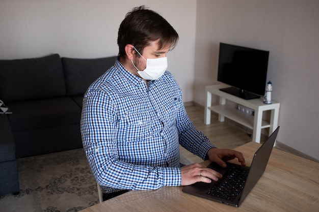 Stare a casa. uomo che indossa una maschera lavorando su da casa il suo computer portatile