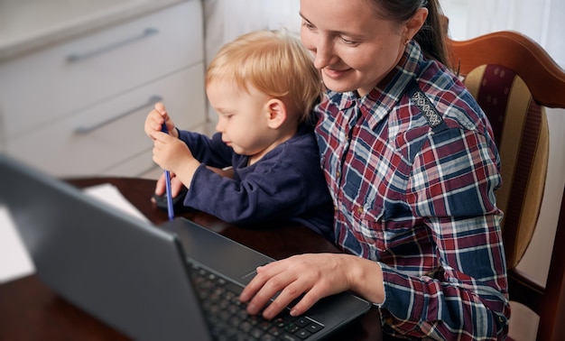 Stay at home mom working remotely on laptop while taking care of her baby