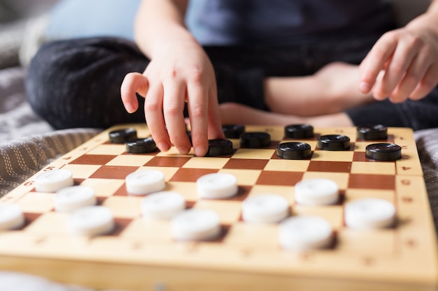 Stay at home Quarantine concept. Young kid hands playing checkers table game on bed. Board game and kids leisure concept. Family time.