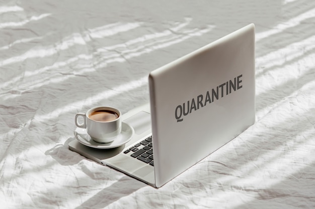 Stay Home, quarantine. Working From Home. 
Laptop and cup of coffee on white bed. Work at home concept. Morning light. Lifestyle Concept