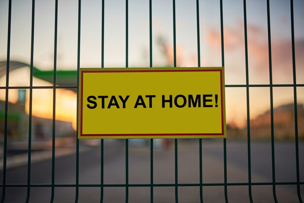 Stay at home sign on a fence with blurred city view