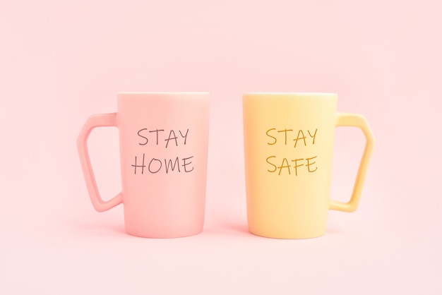 ピンクの背景に2杯のコーヒーに書かれたSTAYHOMEとSTAYSAFE。ヘルスケア、医療、検疫の概念。テキスト用のスペースをコピーする