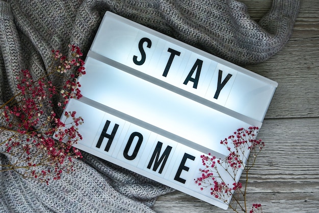 Stay at home. Text in your light box, with a background of sweater and dried flower decoration. Coronavirus devices. Social distancing. Protection against pandemics. White lightbox.