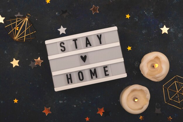 Stay home written on a lightbox among christmas decorations on a dark background. christmas time pandemic concept
