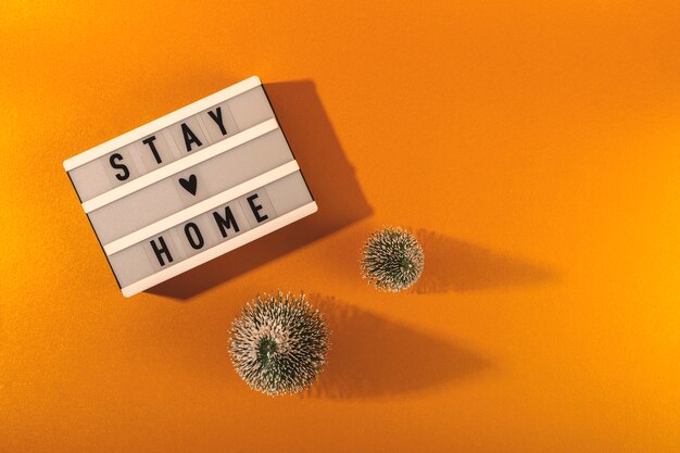 Stay Home written on lightbox among Christmas trees. Christmas pandemic concept layout