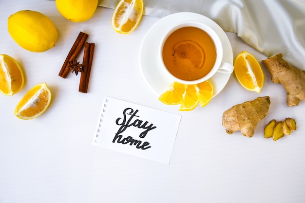 STAY HOME- written on piece of paper among the products for the treatment of common cold - lemon, ginger, chamomile tea. Vitamin natural drink. Cinnamon anise star.
